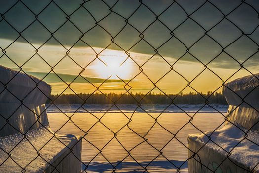 sunset on the river through the bars of the river in the winter