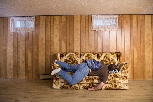 man wearing jeans, sleeping facedown on an old basement couch