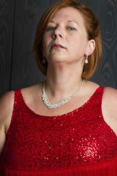 forty something large woman in sparkly dress in front of a blue wood stain background, snobbing the camera