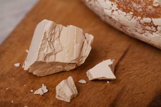 A pile of fresh yeast with a hrannied rustical homemade bread on old cutting board