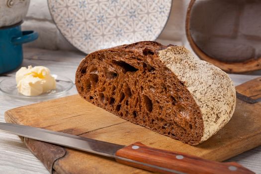 Crannied rustical homemade rye bread on old cutting board with cooking ingredients.