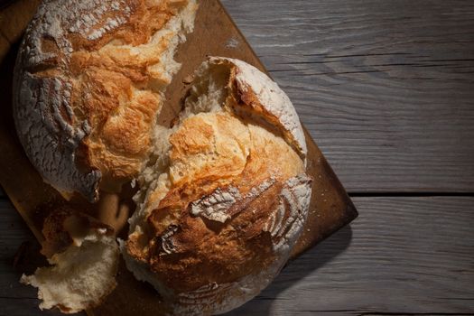 Torned crannied rustical homemade bread loaf on old cutting board over grey wooden table. Dark background with a free space.