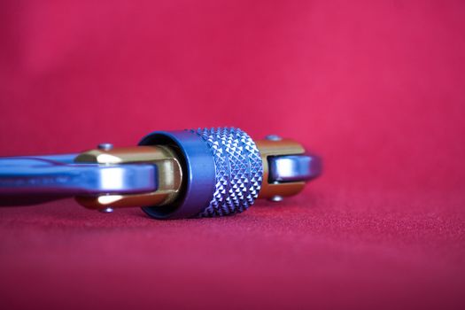 Angle close-up on a locking mechanism of an alluminium climbing carabiner on red background