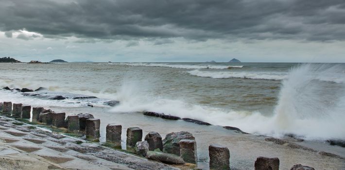 Storm protection concrete coastline defence structure barrier with the ocean beyond and waves hitting the structure. With islands in the background set in the south china sea.