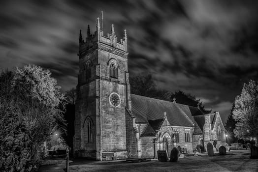 A country village church in the UK taken in black and white mono taken at night from the graveyard