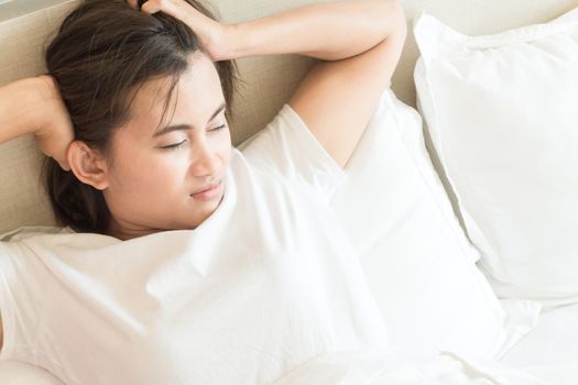 Closeup woman waking up with sore head on bed, health care and medical concept, selective focus