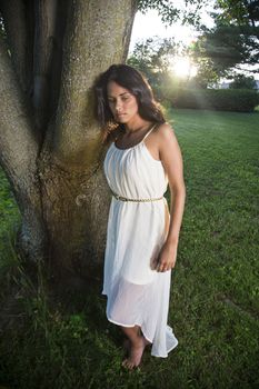 young woman wearing a white dress beside a tree with sad expression
