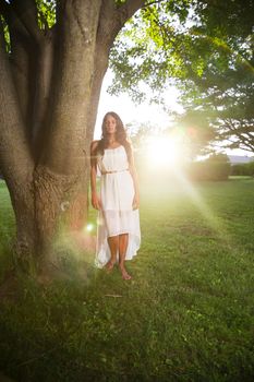 twenty something woman under a tree at sunset, wearing a white dress