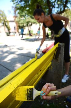 Two girls painting bench in yellow color