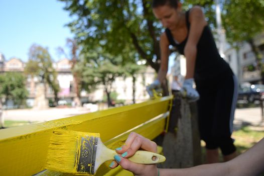 Two girls painting bench in yellow color