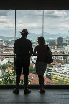 a couple looks at the panorama of Ljubljana from a window