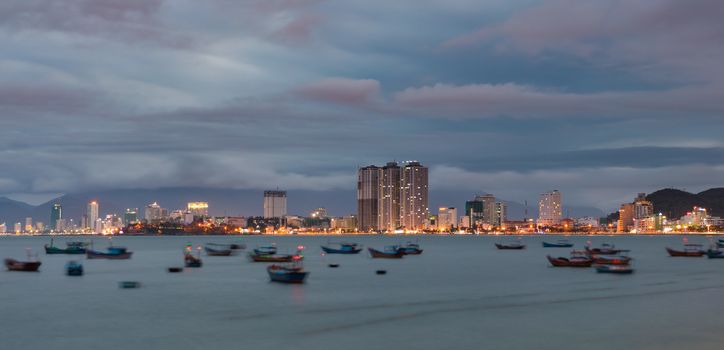 Asian holiday resort Nha Trang Vietnam under a cloudy sunset evening sky from a view point north of the city. With construction development and the city lights ablaze over the fishing boat harbour.