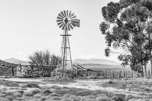 Monochrome water pumping windmill, dam and a kraal on a farm next to the road from Spoegrivier to Klipfontein in the Northern Cape Namaqualand region of South Africa