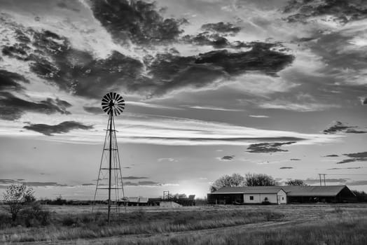 A water-pumping windmill at sunset on a farm near Ritchie in the Northern Cape Province of South Africa. Monochrome