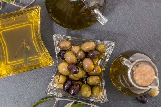 Green and black olives with olive oil bottles on a schist board.