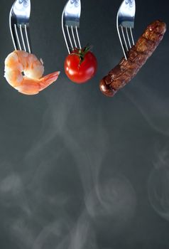 Barbecued ingredients including shrimp and sausage on forks with background space 