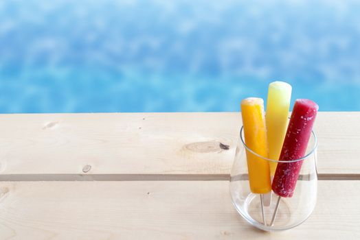 Frozen ice lollies in a glass by a swimming pool