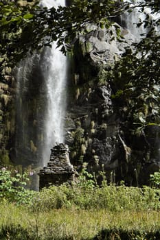 Waterfall in the mountains in Nepal among green plants with old buddist chorten monument