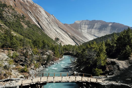 Bridge in mountain valley in nepalese himalayas with huge rock  Sworgadwari