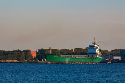 Green cargo ship leaves the port in a clear day