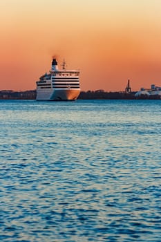 White passenger ship moving against the orange sunset sky