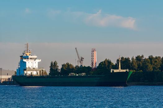 Green cargo ship leaves the port in a clear day