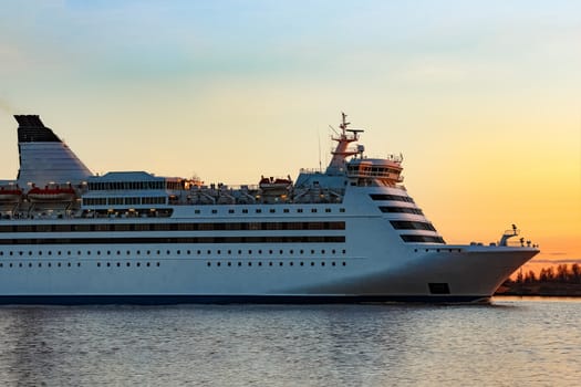 White passenger ship moving against the orange sunset sky