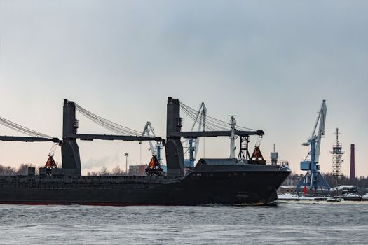 Black bulk carrier sailing to the sea in cold winter
