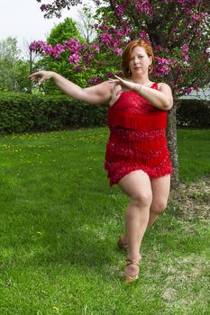 overweight forty year old woman in the middle of a lady styling dance pose, outside under a cherry tree