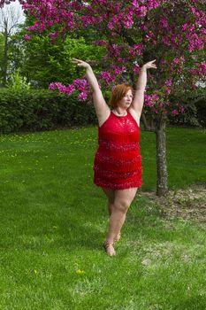 overweight forty year old woman in the middle of a lady styling dance pose, outside under a cherry tree
