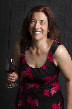 forty year old woman wearing a summer dress, drinking a glass of red wine and laughing