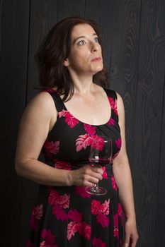 forty year old woman wearing a summer dress, drinking a glass of red wine