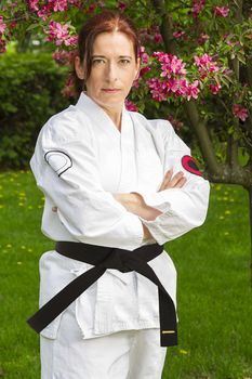 forty year old woman wearing karate gi outside, under a cherry tree in bloom, with arms cross