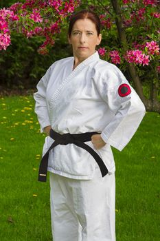 forty year old woman wearing karate gi outside, under a cherry tree in bloom, with arms on her hips