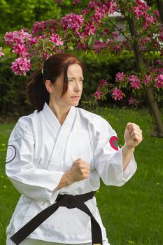 forty year old woman wearing karate gi outside, under a cherry tree in bloom, in striking pose