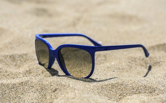 Blue sunglasses on the sand