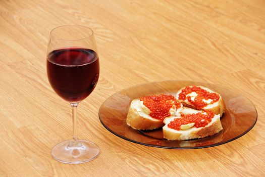 Wine glass with red wine and sandwiches with red caviar on a wooden table.