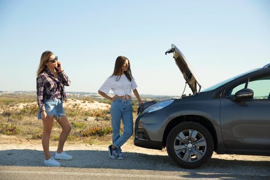 Female friends examining broken down car on country road 