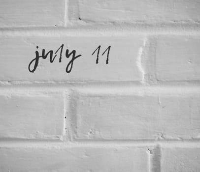 PHOTO OF july 11 WRITTEN ON WHITE PLAIN BRICK WALL