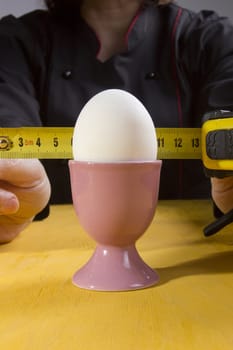 Egg in the holder and hands of the cook with a tape measure