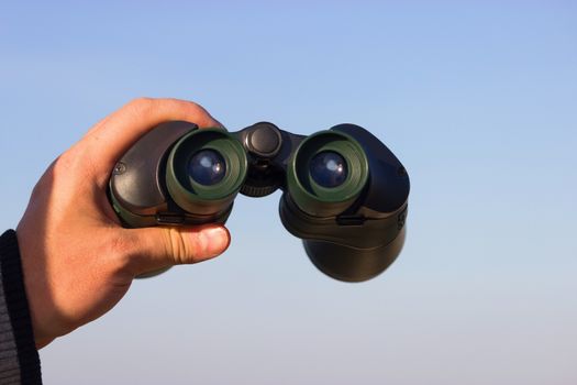 binocular in mans hands on the blue sky background