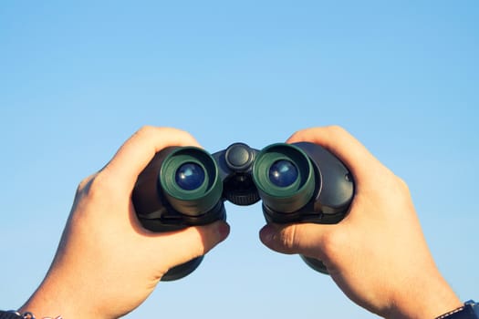 binocular in mans hands on the blue sky background