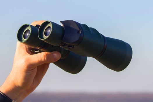 binocular in mans hands on the blue sky background