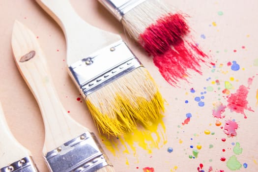 Different sizes paintbrushes against a background of multicolored paint spread.