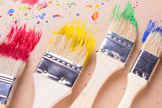 Different sizes paintbrushes against a background of multicolored paint spread.