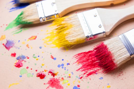 Different sizes paintbrushes against a background of multicolored paint spread.