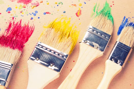 Different sizes paintbrushes against a background of multicolored paint spread.