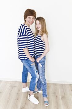 Happiest mother and daughter near white wall in striped clothes