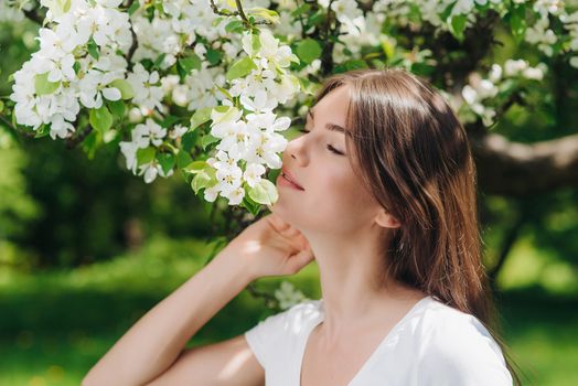 Beautiful young brunette woman standing near blooming apple tree