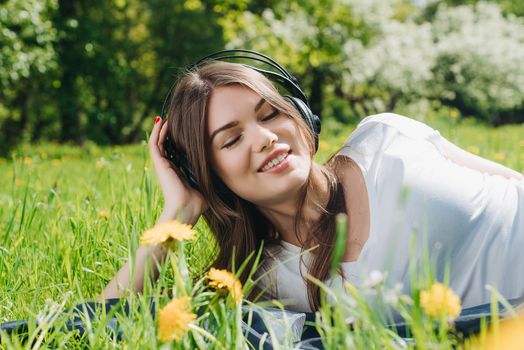 Young brunette woman with headphones listening to the music outdoors on sunny summer day